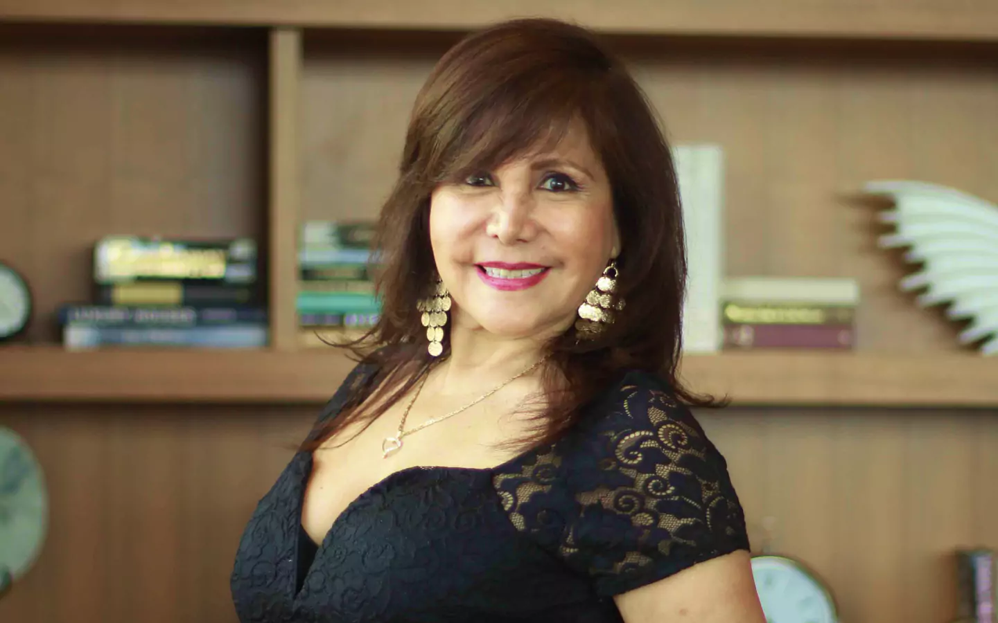 Woman smiling in black lace dress in front of bookshelf